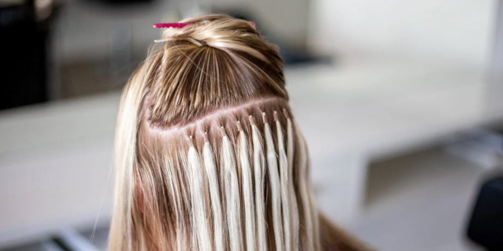 A woman receiving hair styling with Dallas Microbead Extensions while showcasing her pink nails.