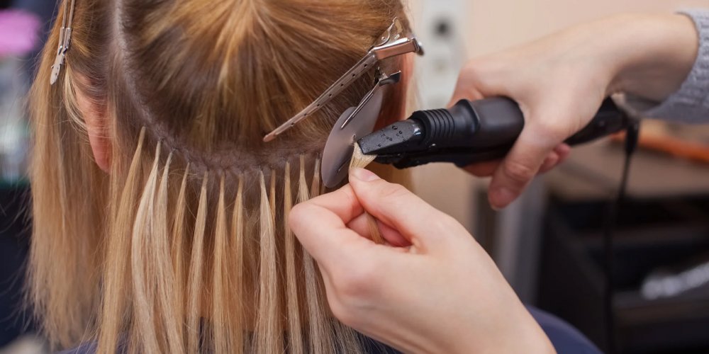 A stylist uses a hair dryer to cut a woman's hair, showcasing Fusion Hair Extensions in a salon setting